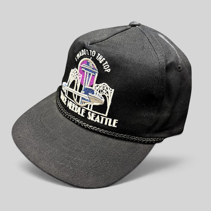 Raree Finds vintage 90s black snapback hat featuring a colorful Seattle Space Needle embroidery and braided rope trim.