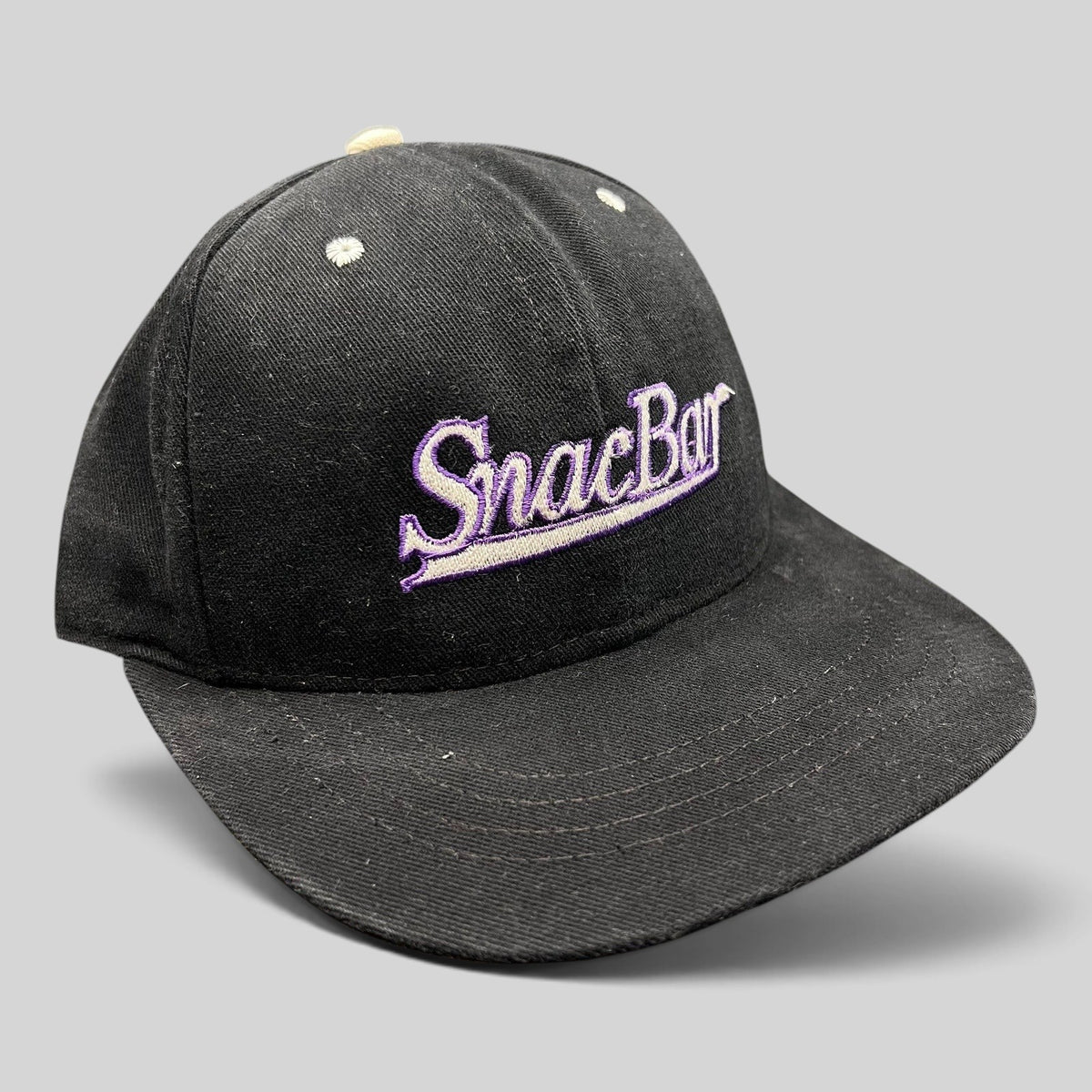 Raree Finds vintage 90s black snapback hat with purple SnacBar script embroidery and a structured front panel.