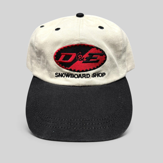 Raree Finds vintage D&E Snowboard Shop two-tone cream and black cotton strapback hat with embroidered front logo.