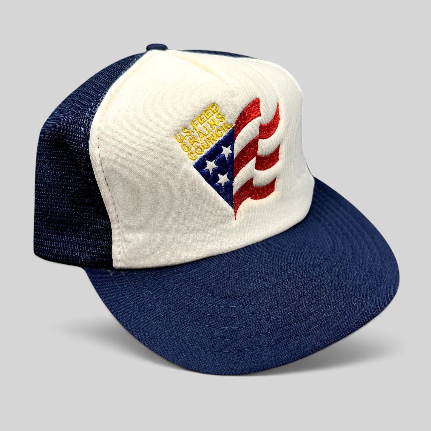 Raree Finds vintage U.S. Feed Grains Council trucker hat with a white foam front, navy mesh back, and flag embroidery.