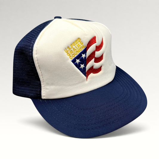 Raree Finds vintage U.S. Feed Grains Council trucker hat with a white foam front, navy mesh back, and flag embroidery.