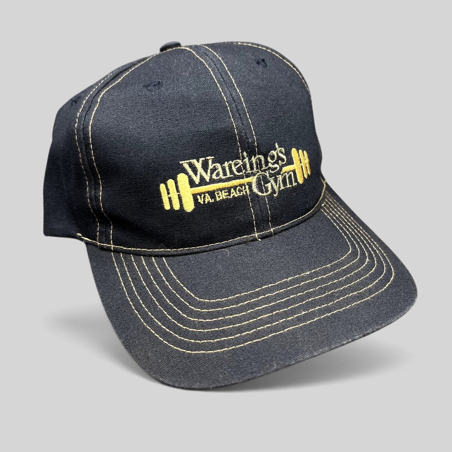 Raree Finds vintage navy blue Wareing’s Gym snapback hat with gold embroidered barbell logo and contrast stitching.