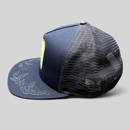 Raree Finds Volcom x New Era 9FIFTY navy trucker hat with embroidered leaf brim detail and mesh back panels.