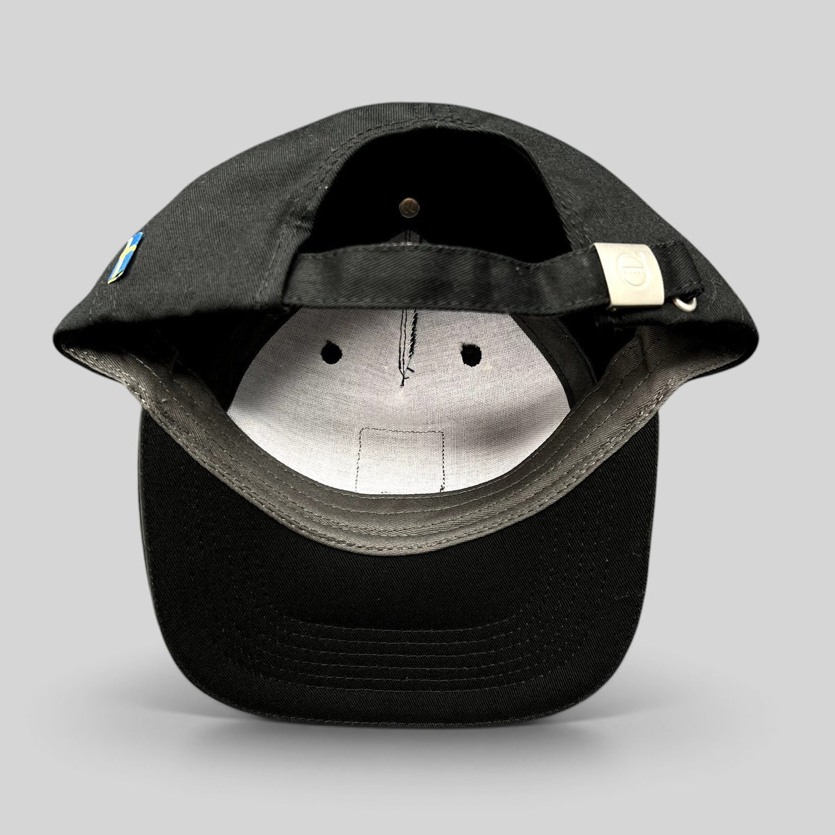 Raree Finds black organic cotton Volvo hat showing the adjustable strap with brushed metal buckle and Swedish flag tag