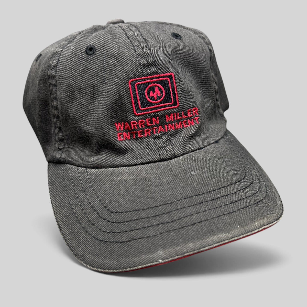 Raree Finds vintage black Flexfit hat with red Warren Miller Entertainment logo embroidery and contrast brim piping.