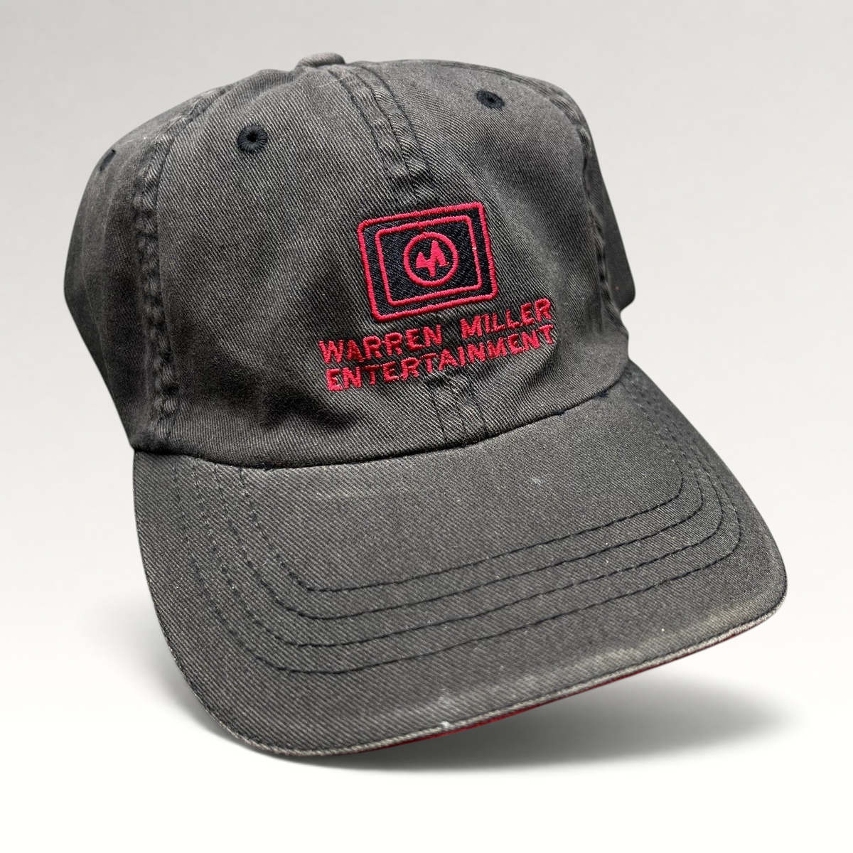 Raree Finds vintage black Flexfit hat with red Warren Miller Entertainment logo embroidery and contrast brim piping.