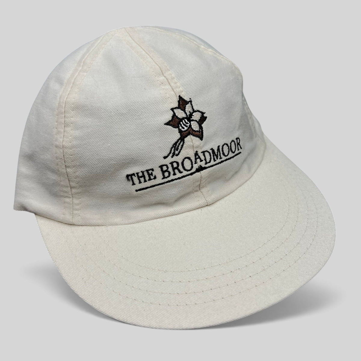 Raree Finds white cotton strapback hat featuring The Broadmoor floral logo and script embroidery