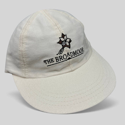 Raree Finds white cotton strapback hat featuring The Broadmoor floral logo and script embroidery