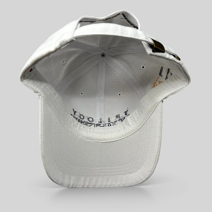 Raree Finds white cotton strapback cap with brass buckle and interior Trilogy branding, viewed from the back.