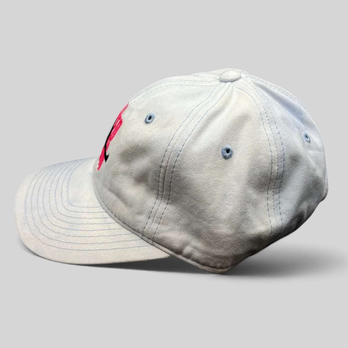 Raree Finds white cotton strapback hat with pink The Naked Gun embroidery and light blue stitching, side view.