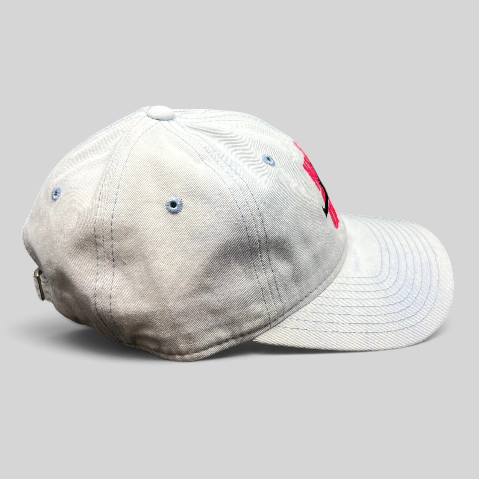 Raree Finds white cotton strapback hat with pink The Naked Gun embroidery and light blue stitching, side view.