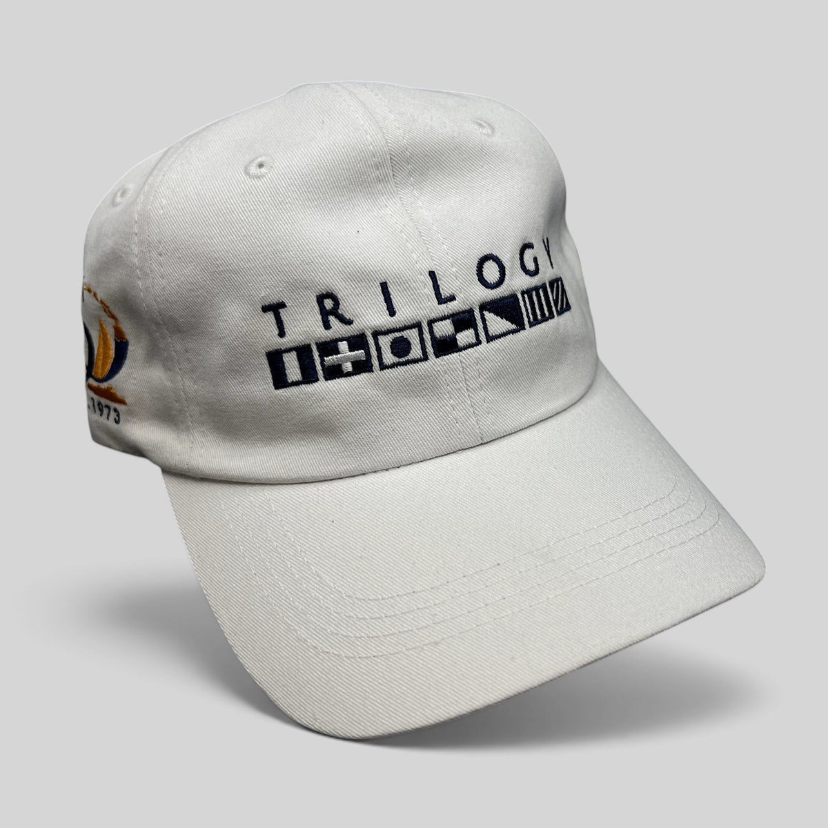 Raree Finds white cotton strapback cap featuring Trilogy branding and embroidered nautical signal flags