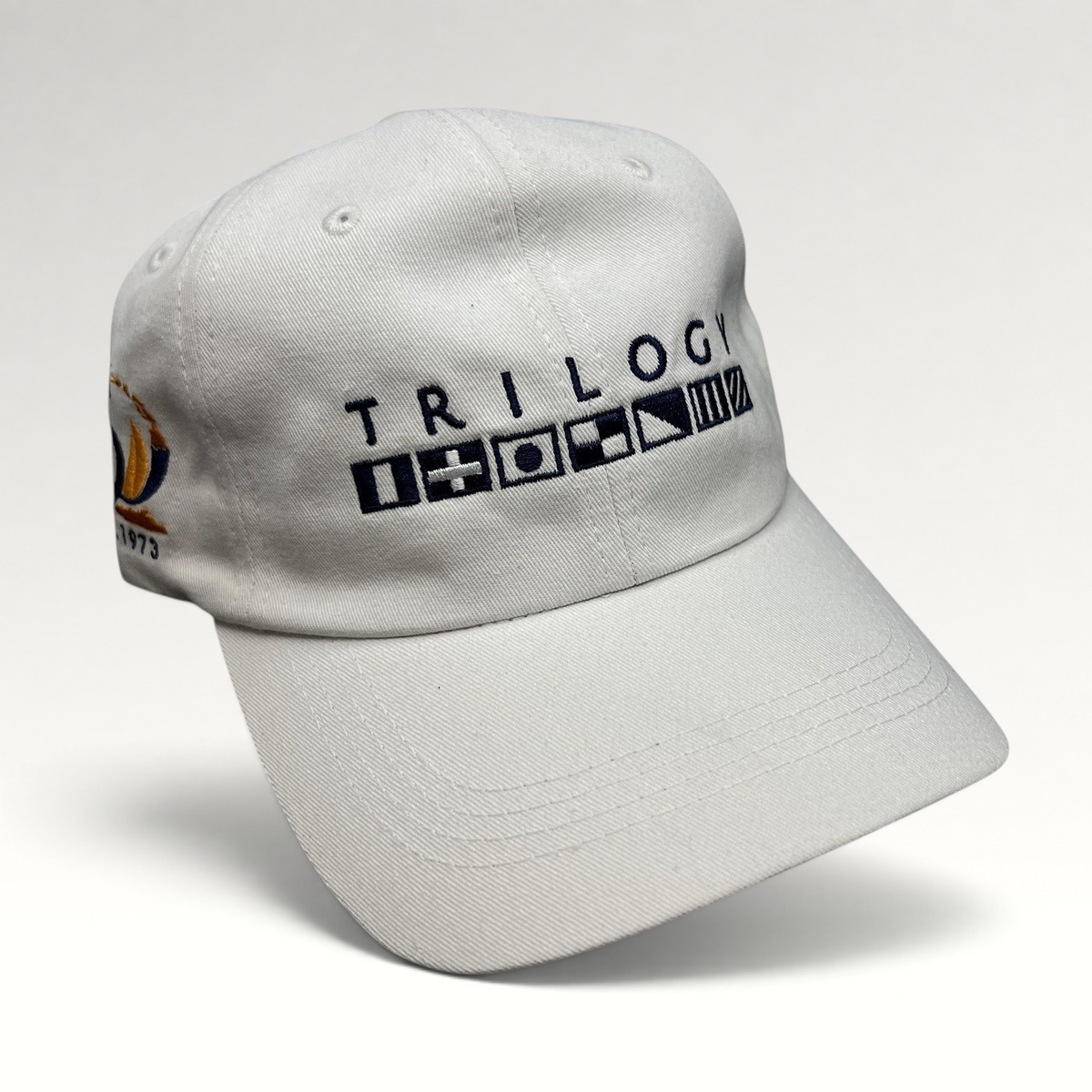 Raree Finds white cotton strapback cap featuring Trilogy branding and embroidered nautical signal flags