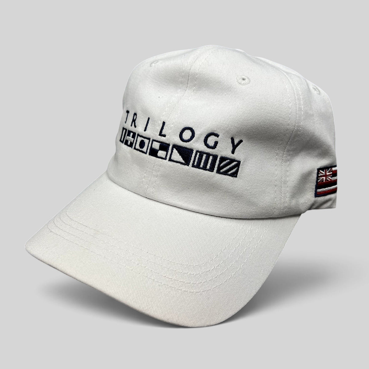Raree Finds white cotton strapback cap with Trilogy branding and embroidered nautical signal flags on the front.