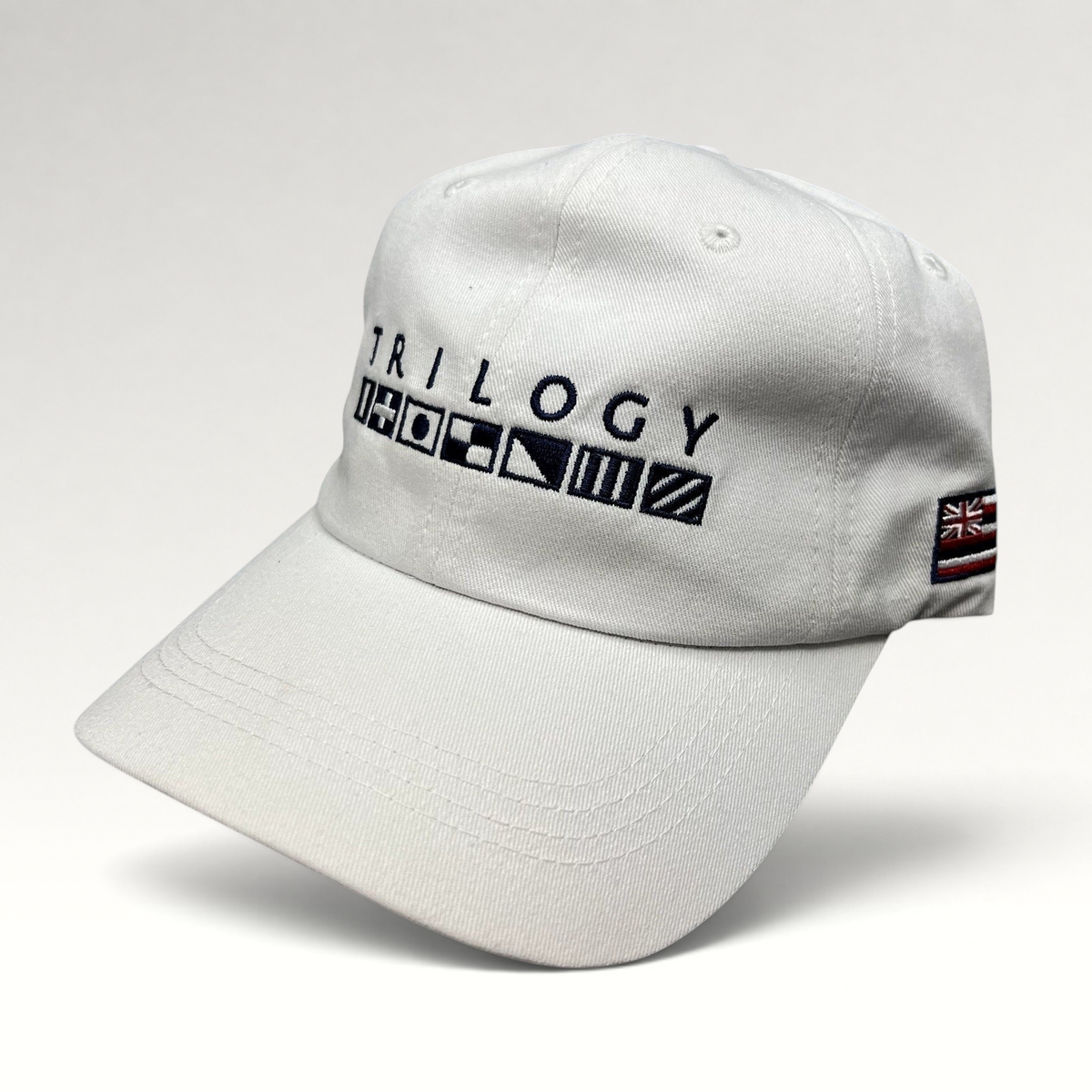 Raree Finds white cotton strapback cap with Trilogy branding and embroidered nautical signal flags on the front.