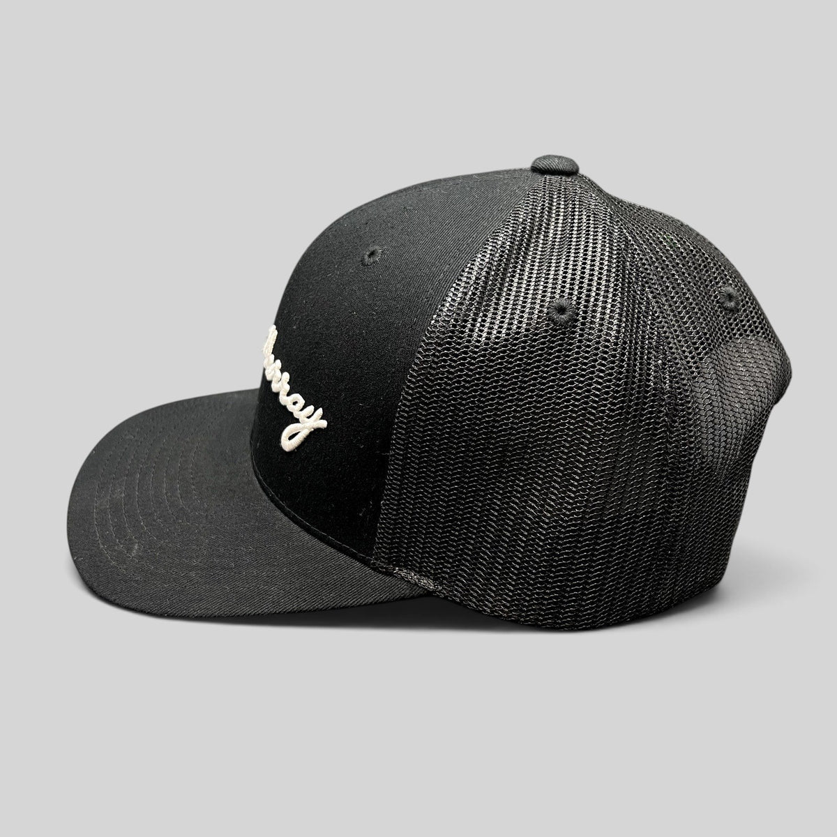 Raree Finds black William Murray Golf trucker hat with white script logo and mesh back panels, side profile view.