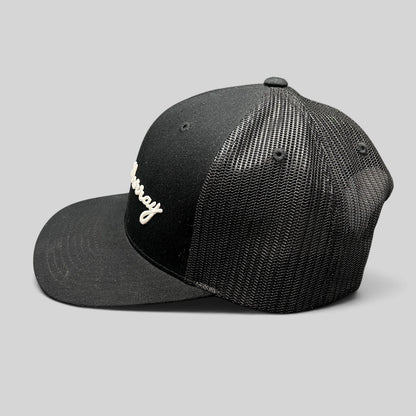 Raree Finds black William Murray Golf trucker hat with white script logo and mesh back panels, side profile view.