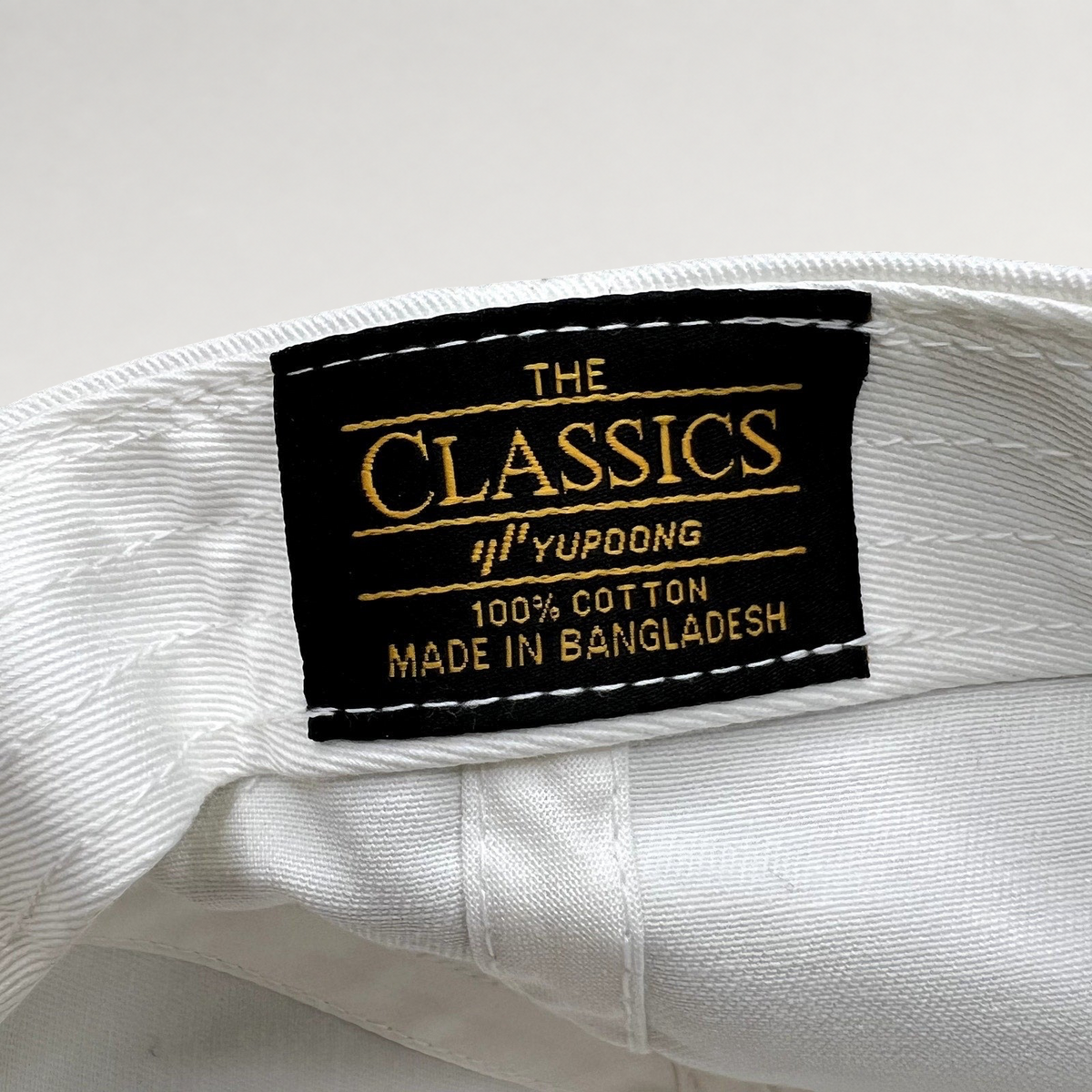 Raree Finds white cotton strapback hat interior featuring a black Yupoong Classics brand tag with gold embroidery
