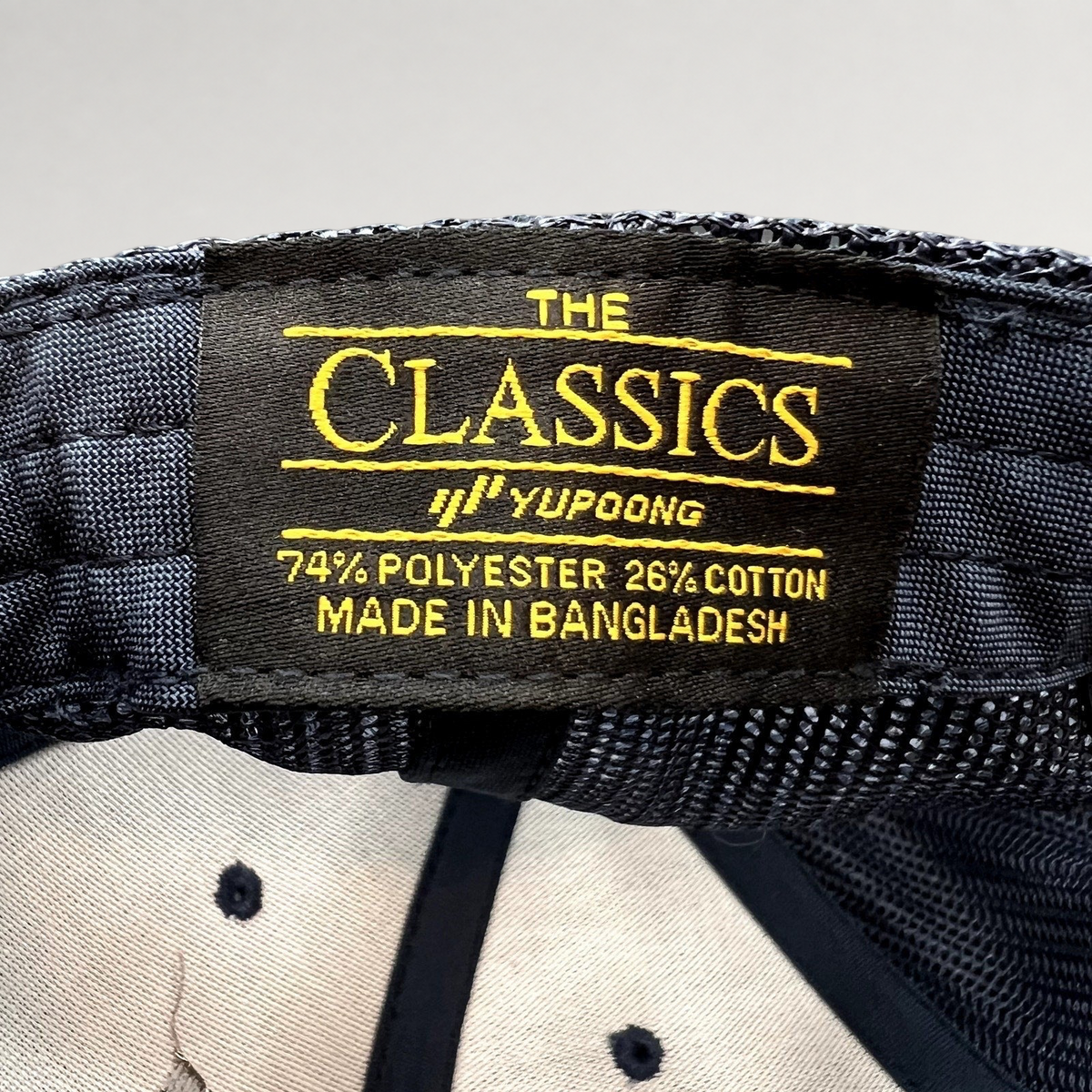 Raree Finds navy blue trucker hat interior label showing Yupoong Classics branding and material composition details.