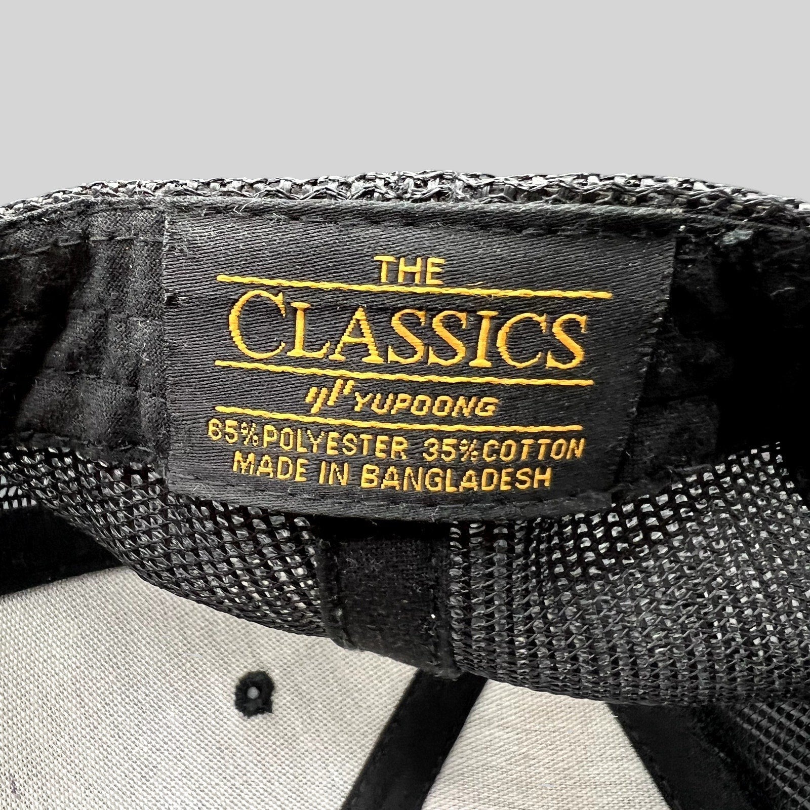 Raree Finds black Yupoong Classics trucker hat interior tag showing material composition and manufacturing origin
