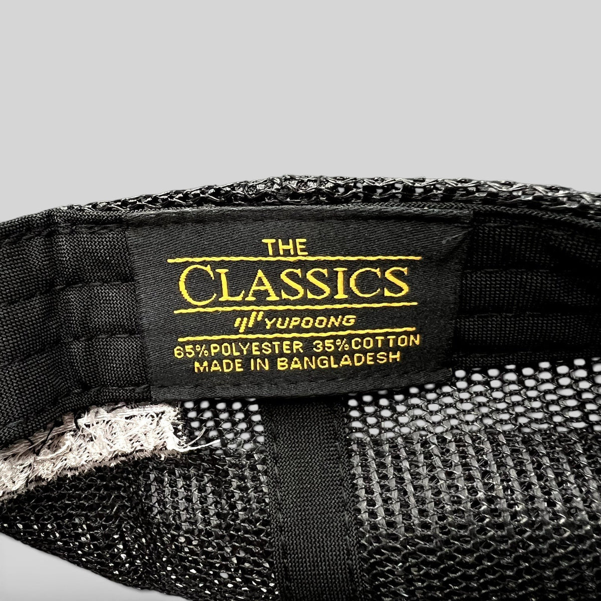 Raree Finds Yupoong Classics black trucker hat interior label showing material composition and brand details