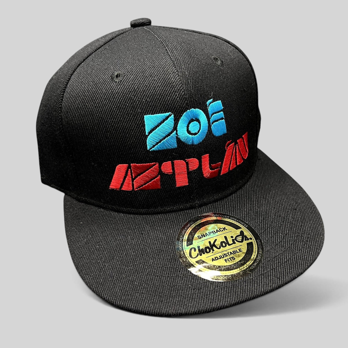 Raree Finds black Chokolids snapback hat featuring embroidered turquoise and red Zoé Aztlán album logo on flat bill