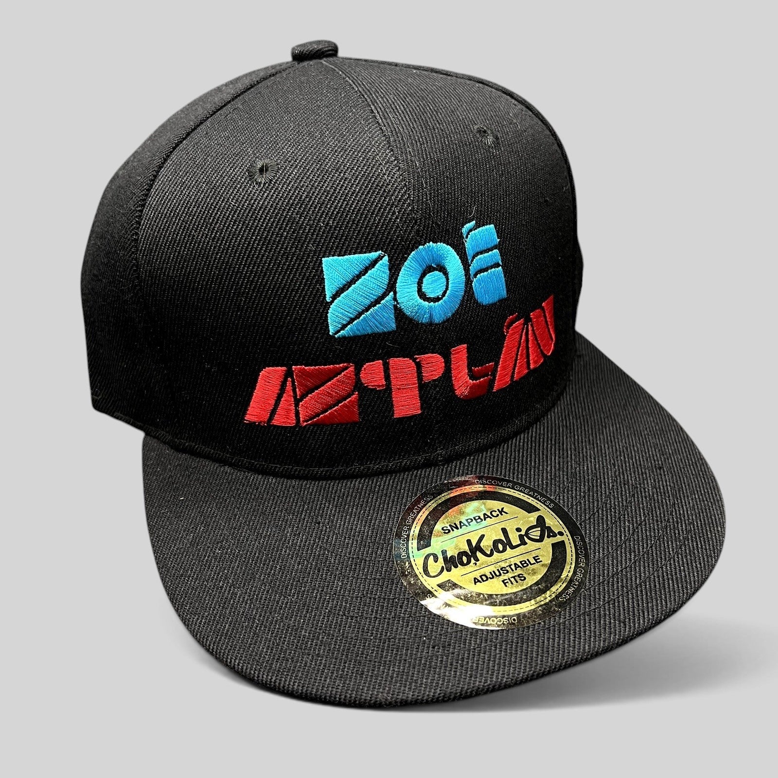 Raree Finds black Chokolids snapback hat featuring embroidered turquoise and red Zoé Aztlán album logo on flat bill
