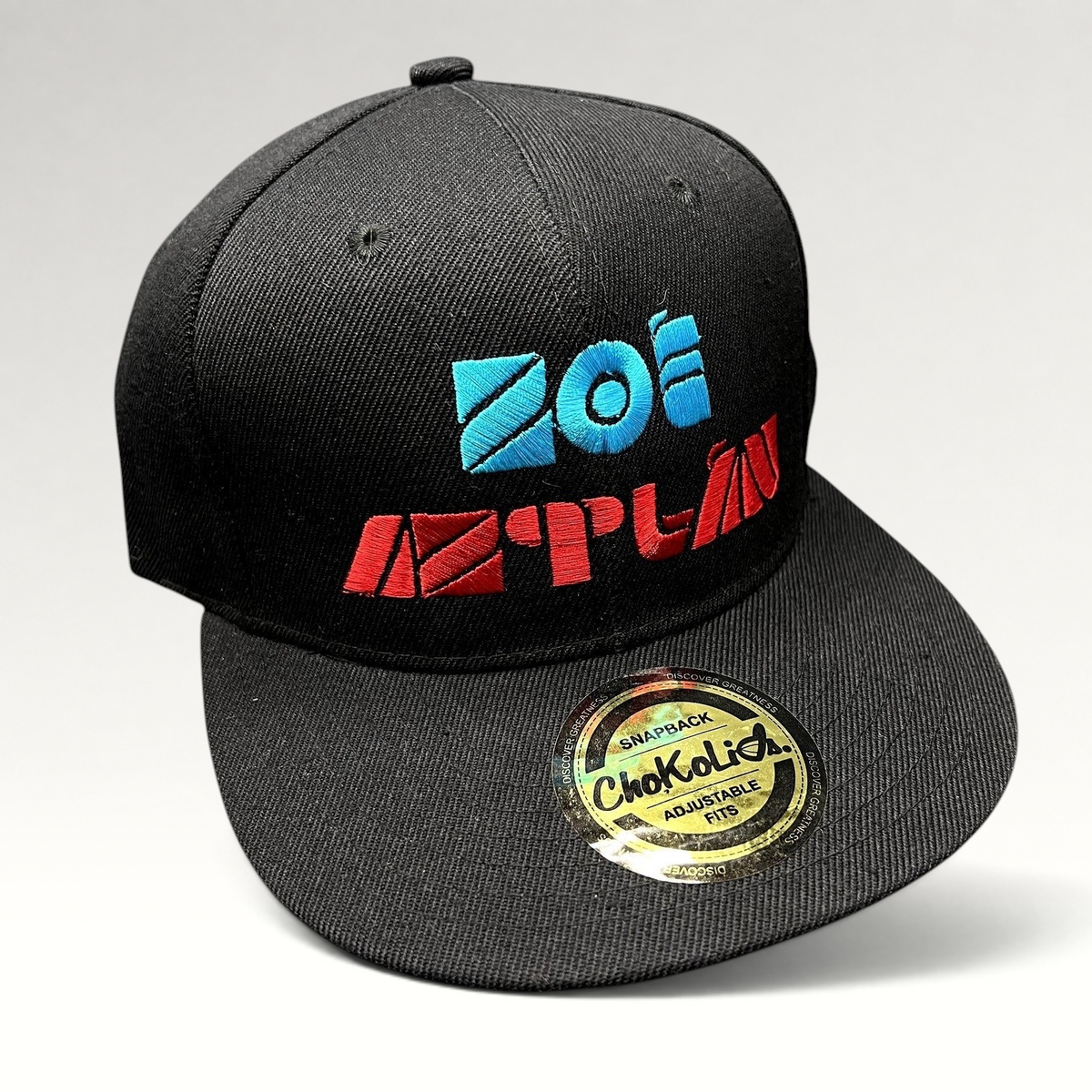 Raree Finds black Chokolids snapback hat featuring embroidered turquoise and red Zoé Aztlán album logo on flat bill
